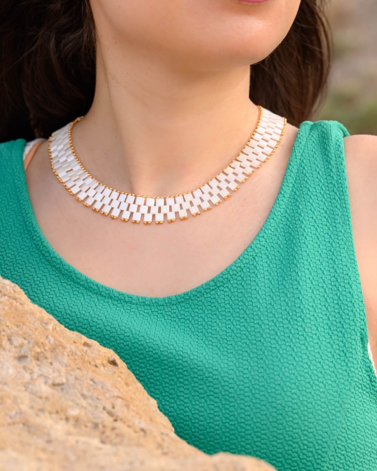 Close-up of a woman wearing a Miyuki necklace featuring antique ivory pearl beads, set against a green top